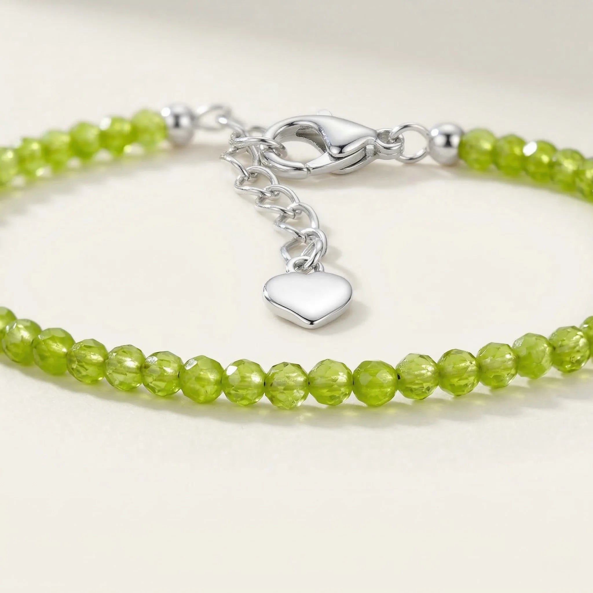 Green beaded bracelet with a silver heart charm on a white background