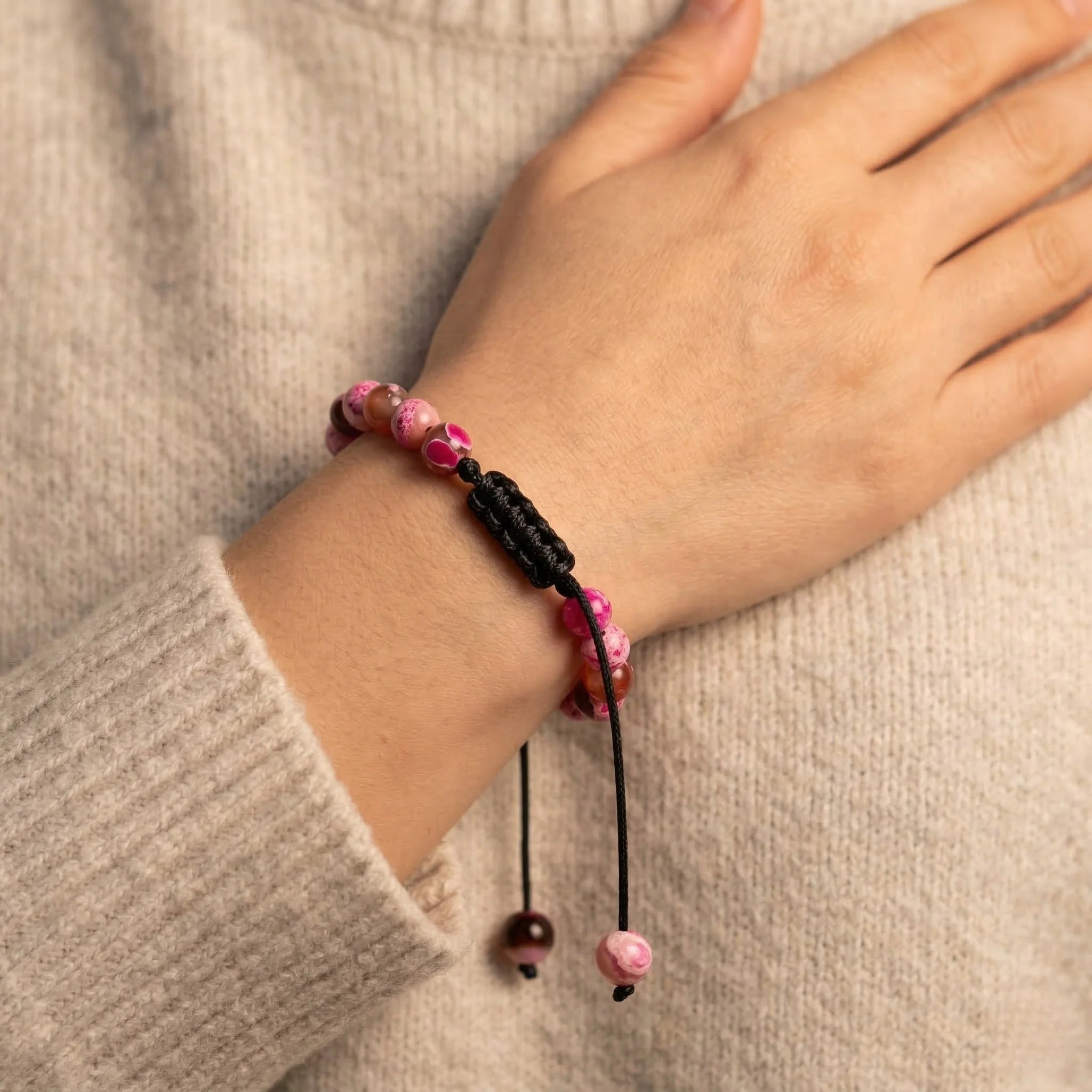 Hand wearing a bracelet with pink beads on a beige background