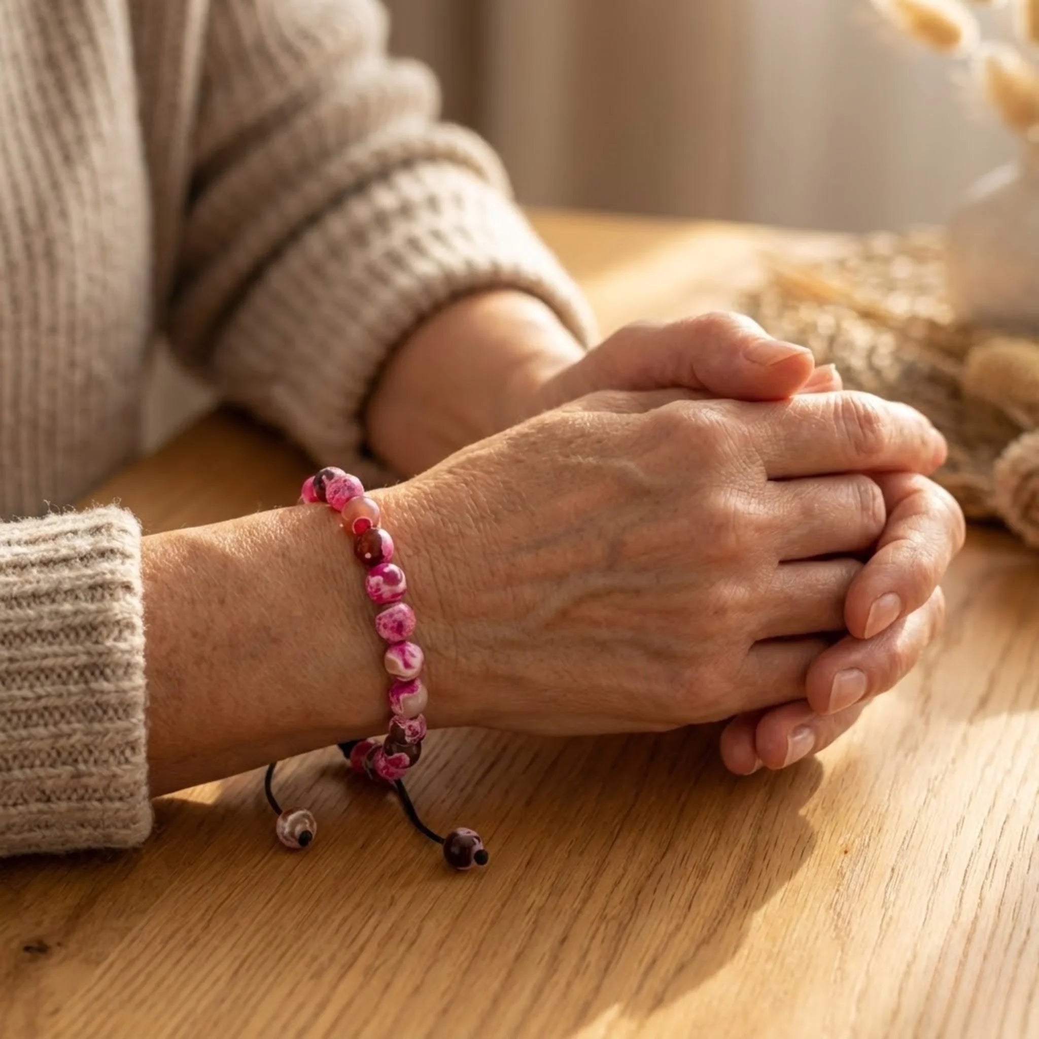 Close-up of hands with a pink beaded Adjustable balance bracelet crafted with pink jasper beads on a braided cord for a soft, expressive style bracelet on a wooden surface