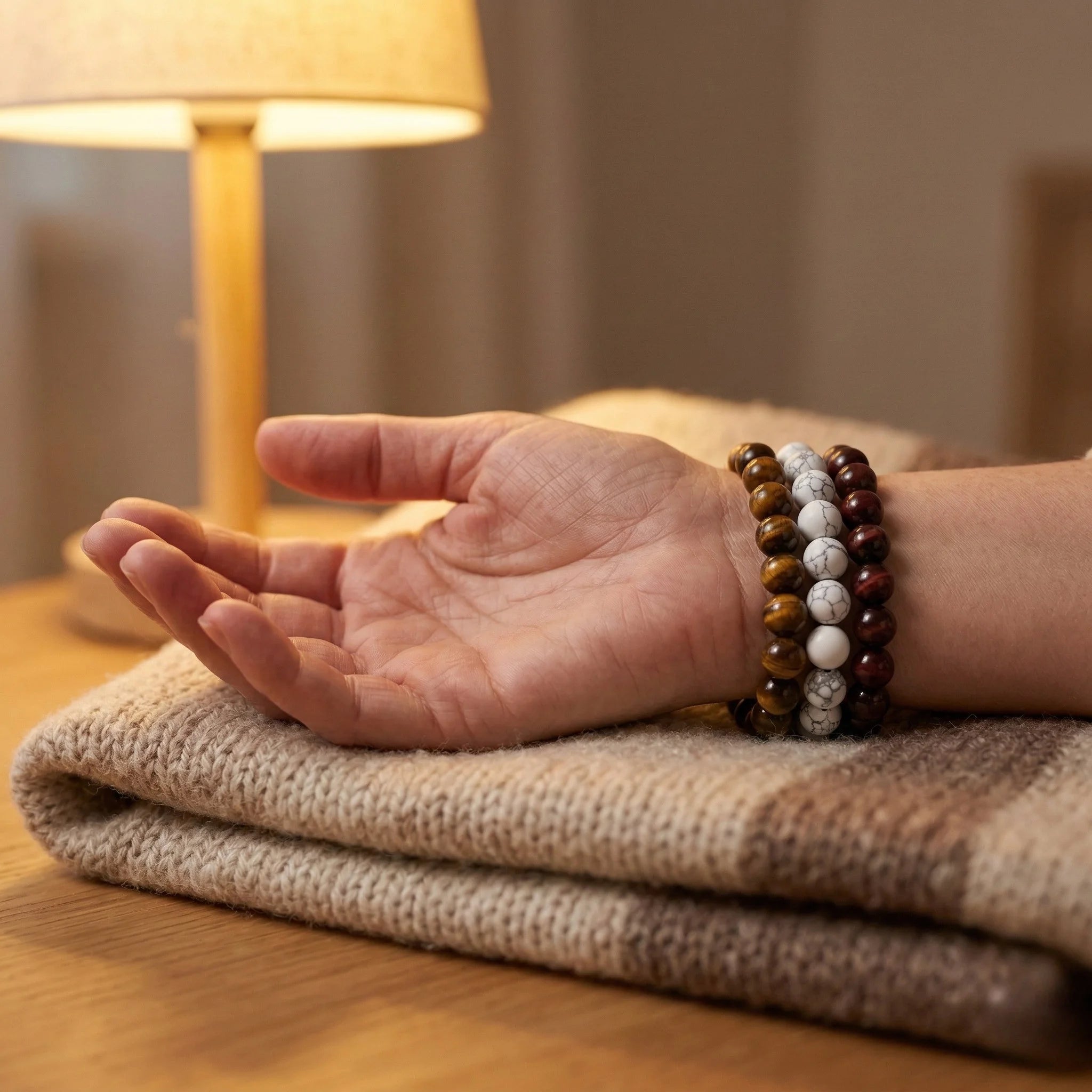 Hand wearing a bracelet with beads on a textured surface, with a lamp in the background