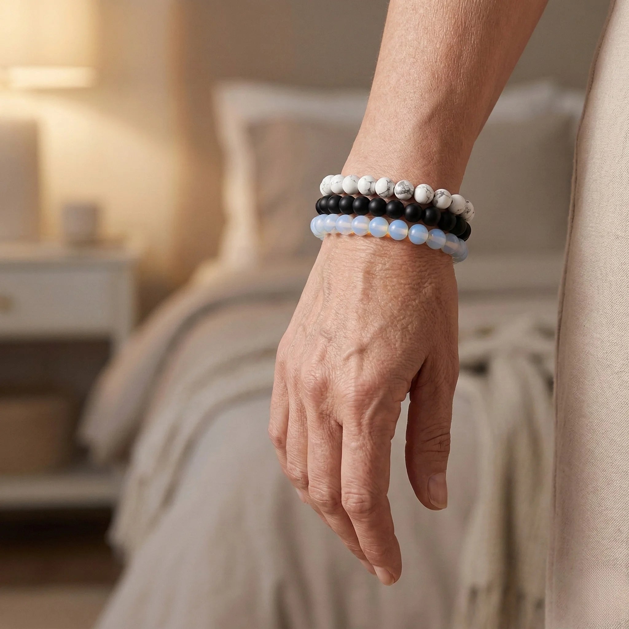 Hand wearing three beaded bracelets with a blurred bedroom background