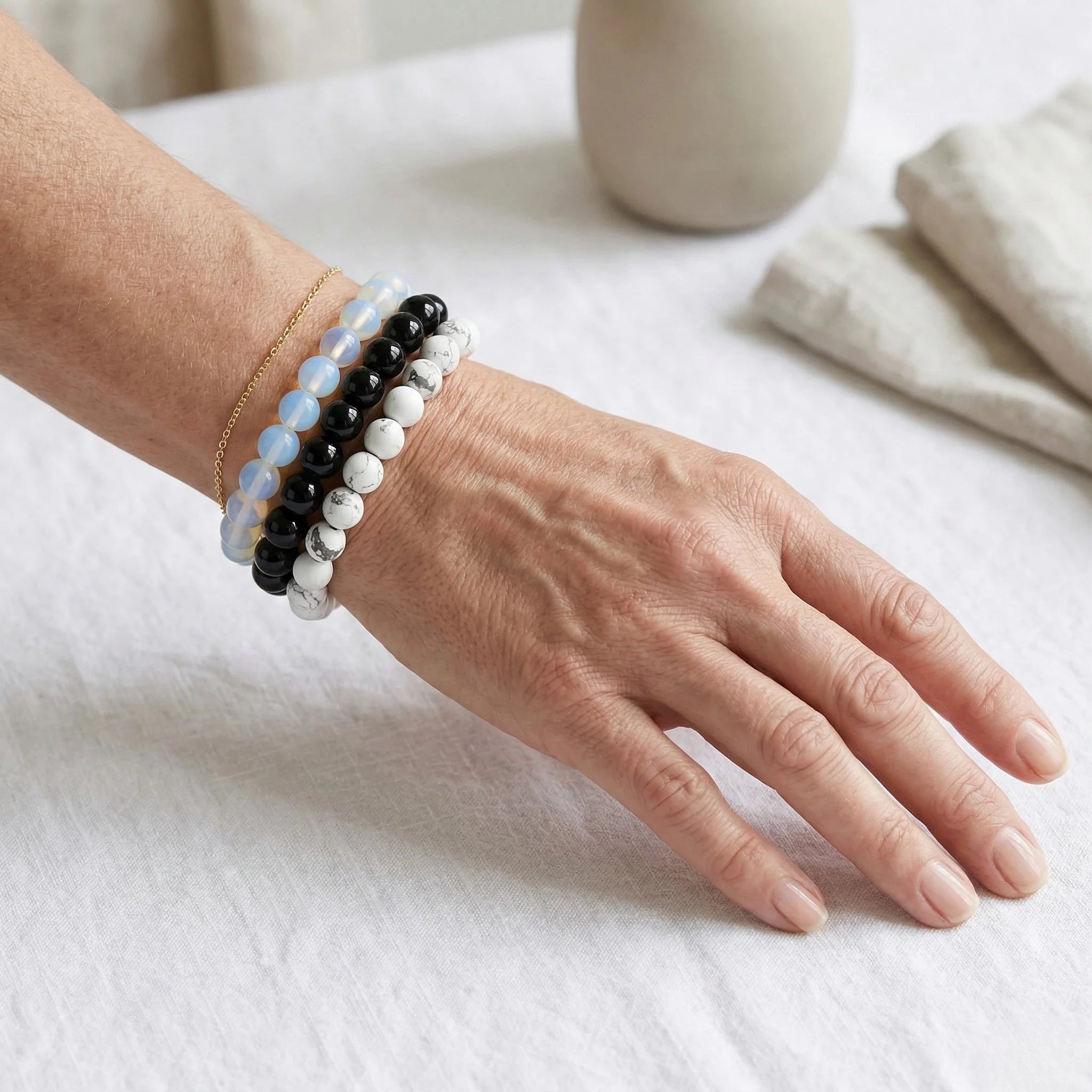 Hand wearing multiple beaded bracelets on a light surface