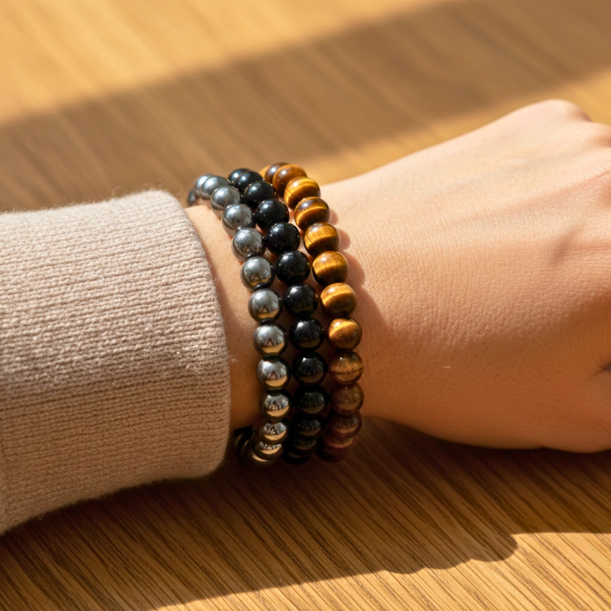 Close-up of a wrist wearing multiple beaded Strength intention bracelet stack featuring tiger eye, black onyx, and hematite beads symbolizing confidence and stability bracelets on a wooden surface