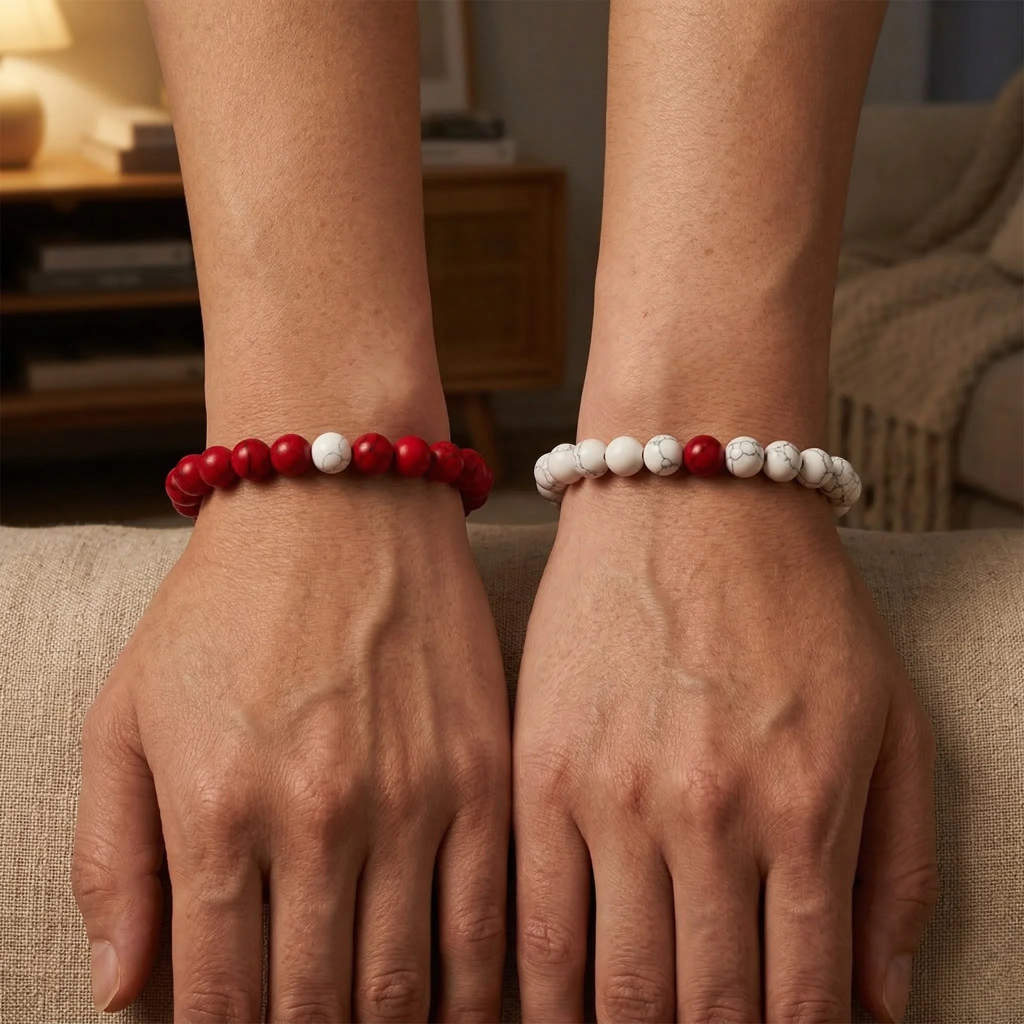 Two hands wearing red and white beaded bracelets on a neutral background