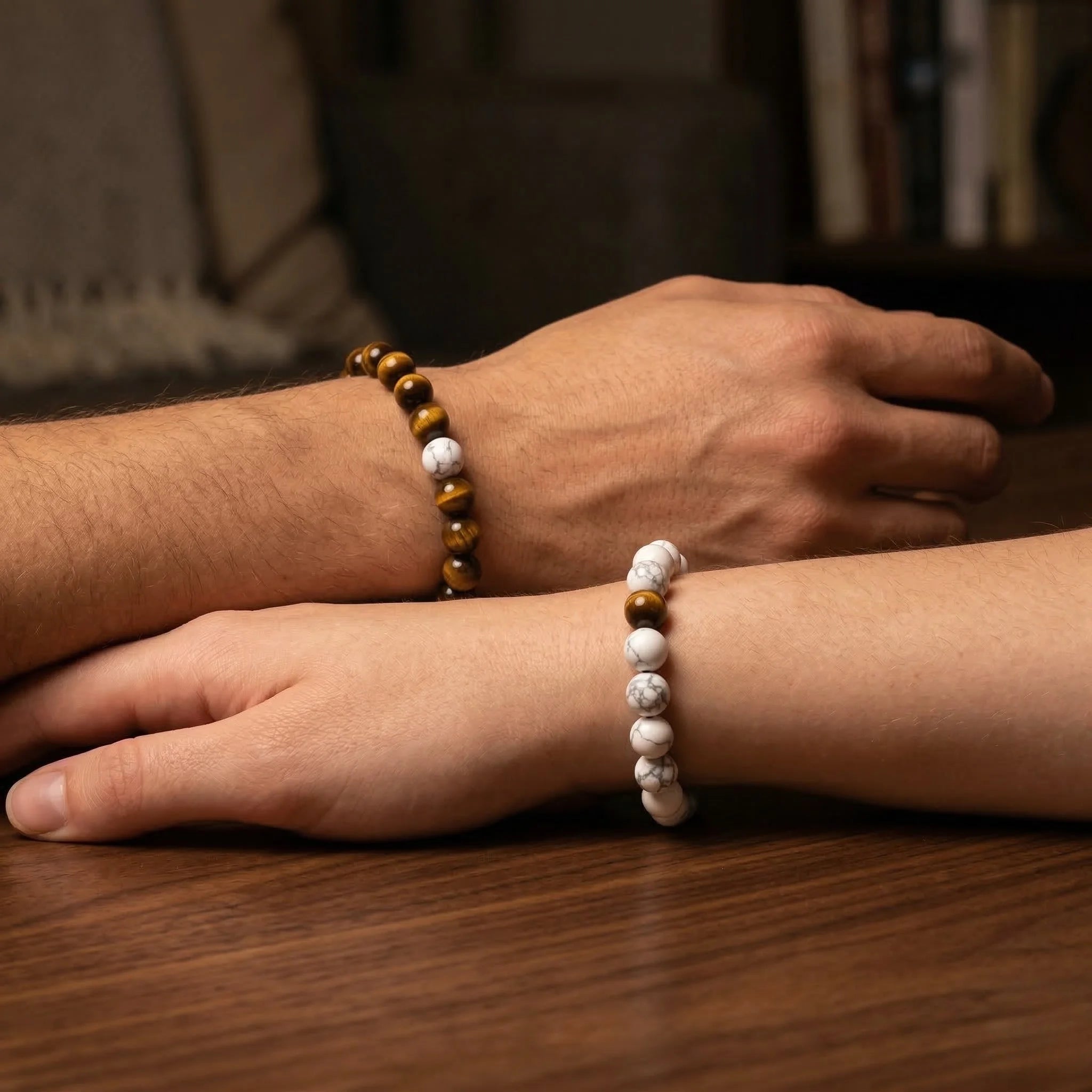 Two hands wearing beaded bracelets on a wooden surface