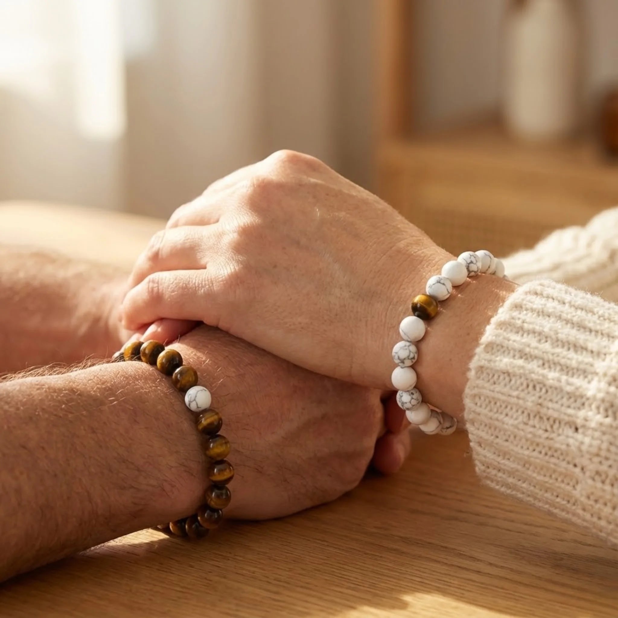 Two hands holding each other with beaded bracelets on a wooden surface.