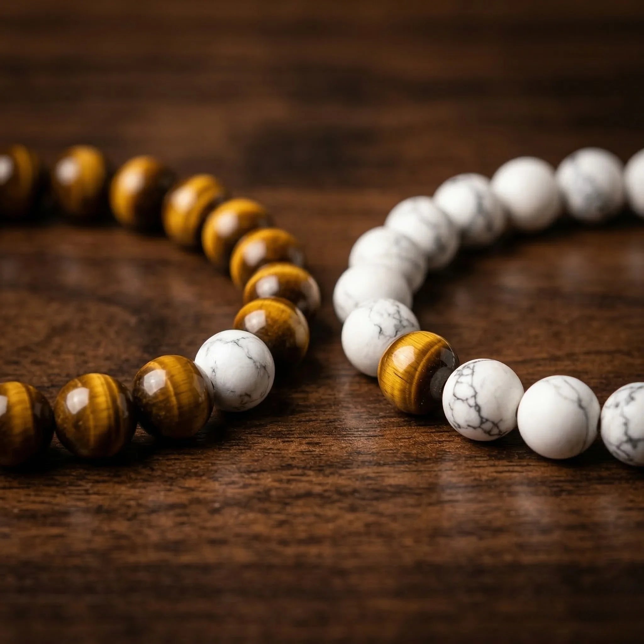 Two beaded bracelets, one with brown and white beads and the other with white beads, on a wooden surface.