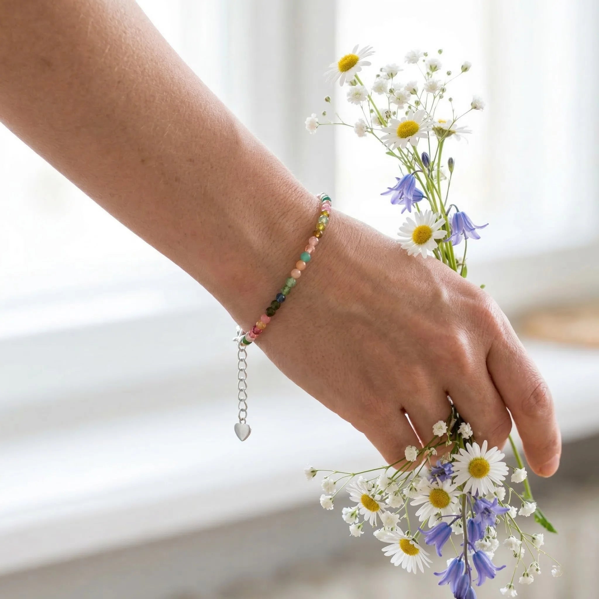 Hand wearing a colorful beaded bracelet holding flowers against a blurred background