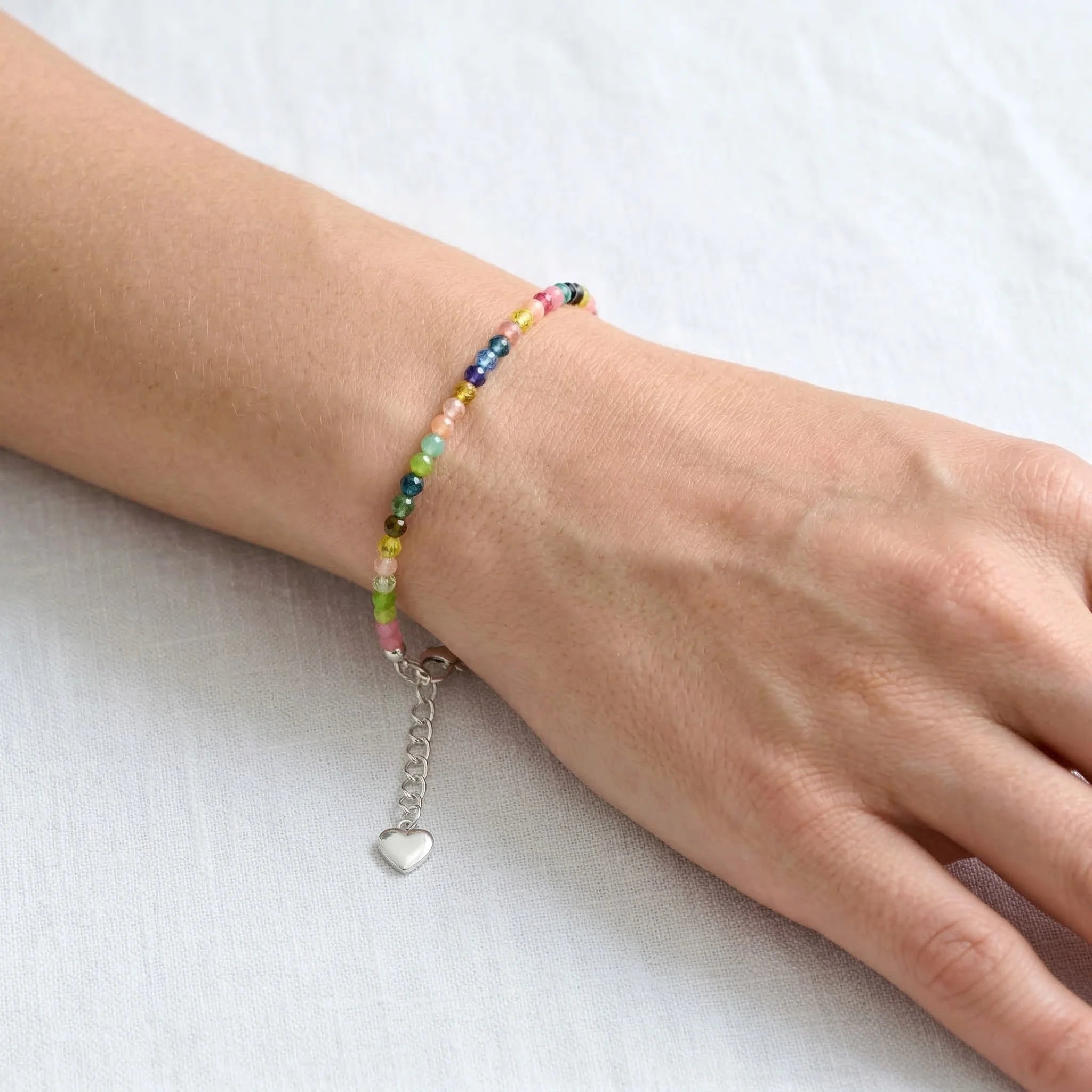Multicolored beaded bracelet with a heart charm on a wrist against a white background