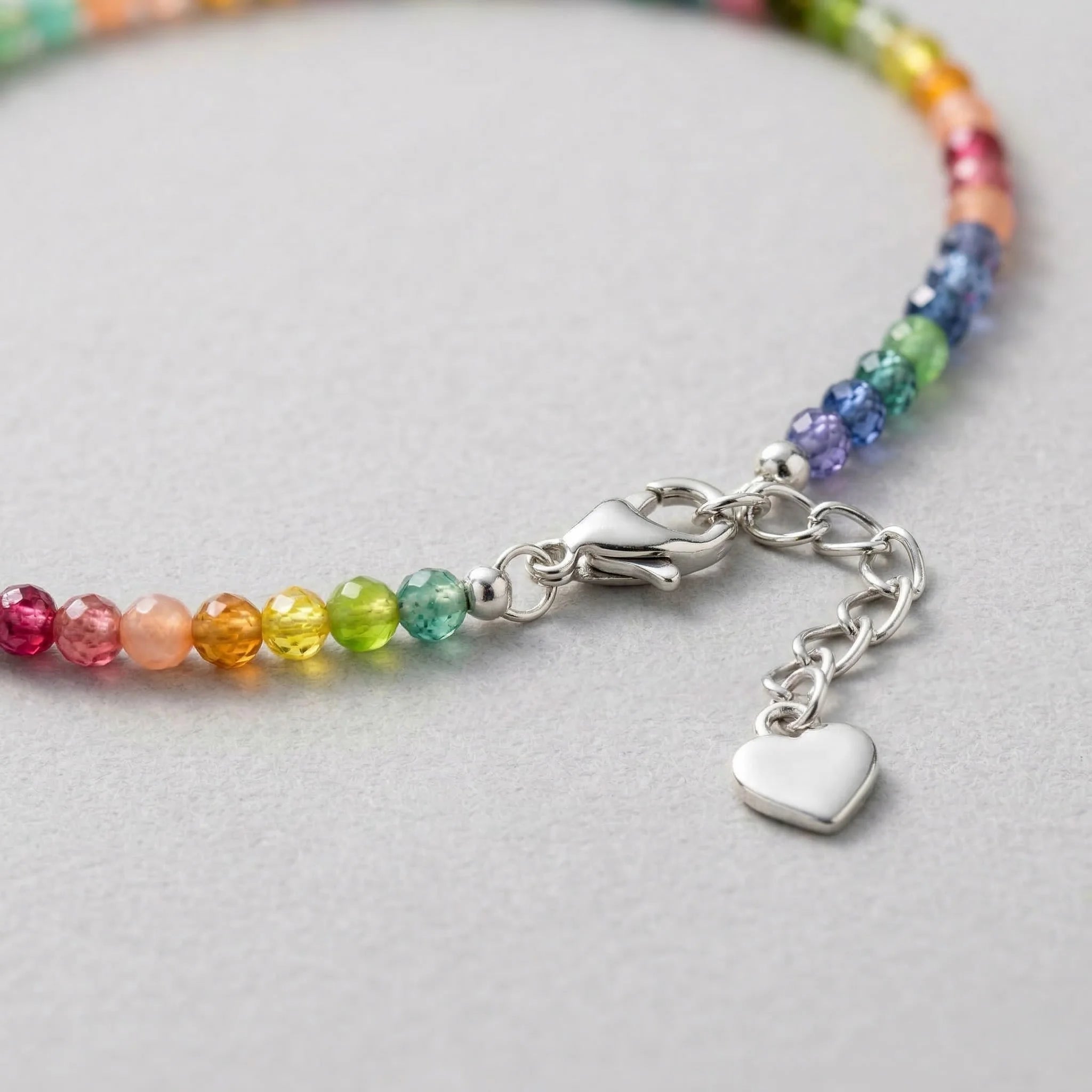 Multicolored beaded bracelet with a silver clasp and heart charm on a light gray background