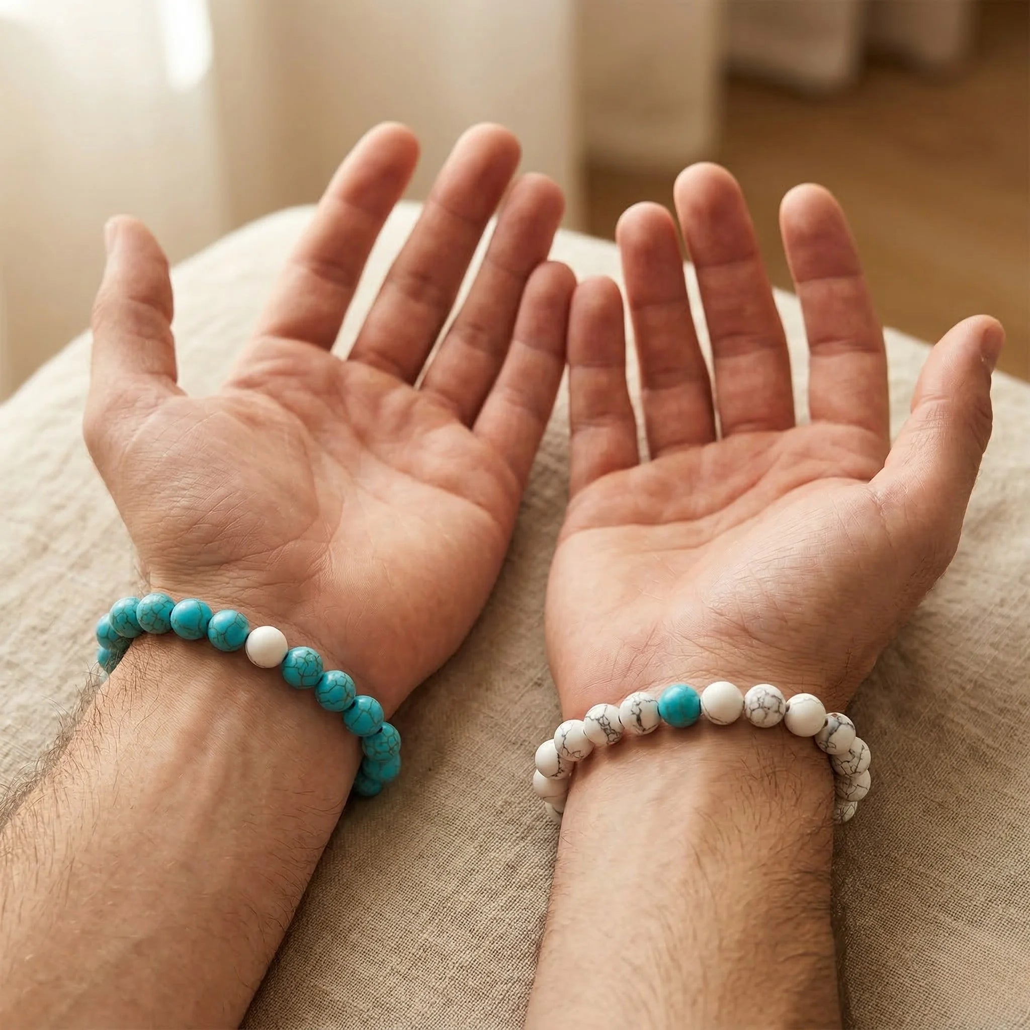 Two hands wearing turquoise and white beaded bracelets on a neutral background