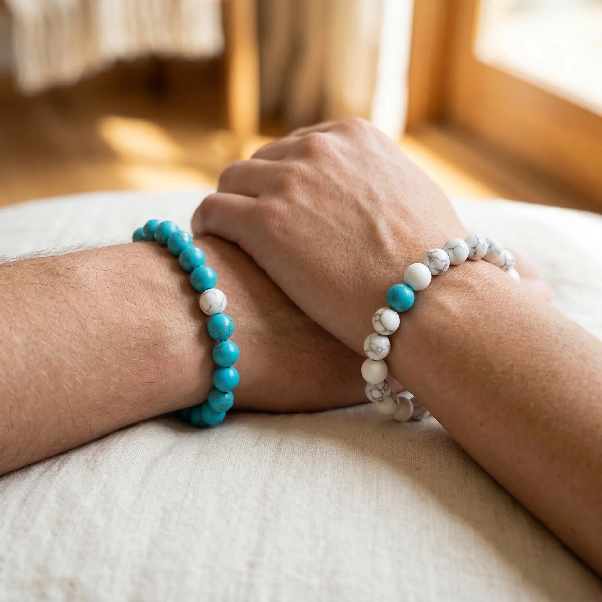 Two hands wearing turquoise and white beaded bracelets on a light surface.
