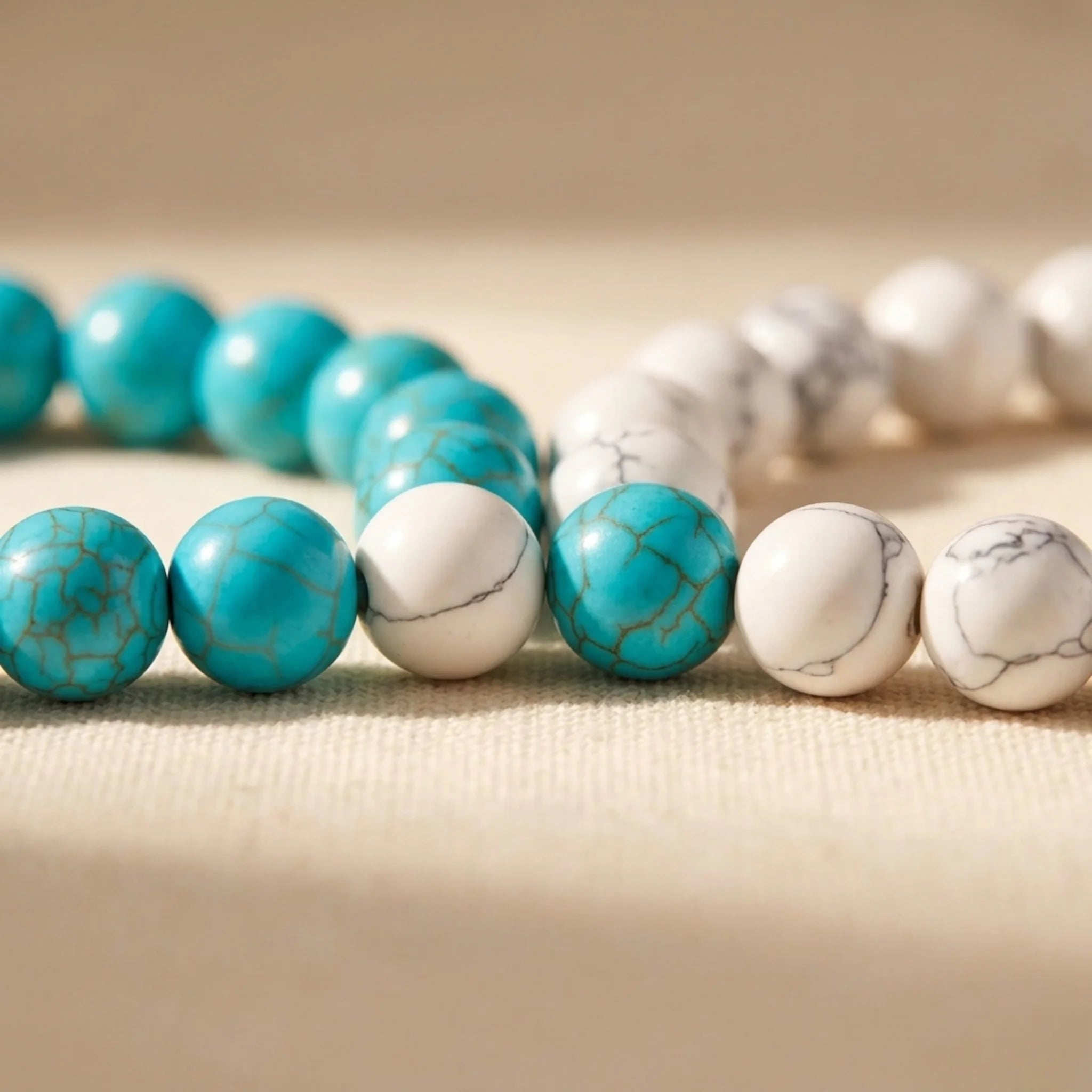 Two bracelets with turquoise and white beads on a beige fabric background