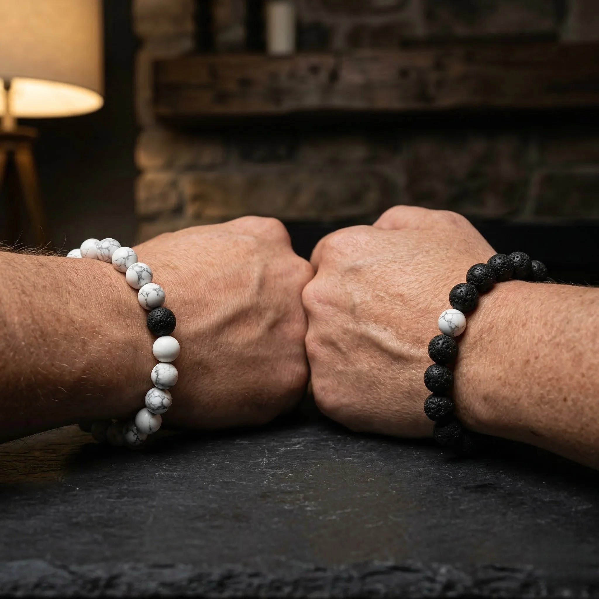 Two hands clasping together wearing black and white beaded bracelets on a dark surface.