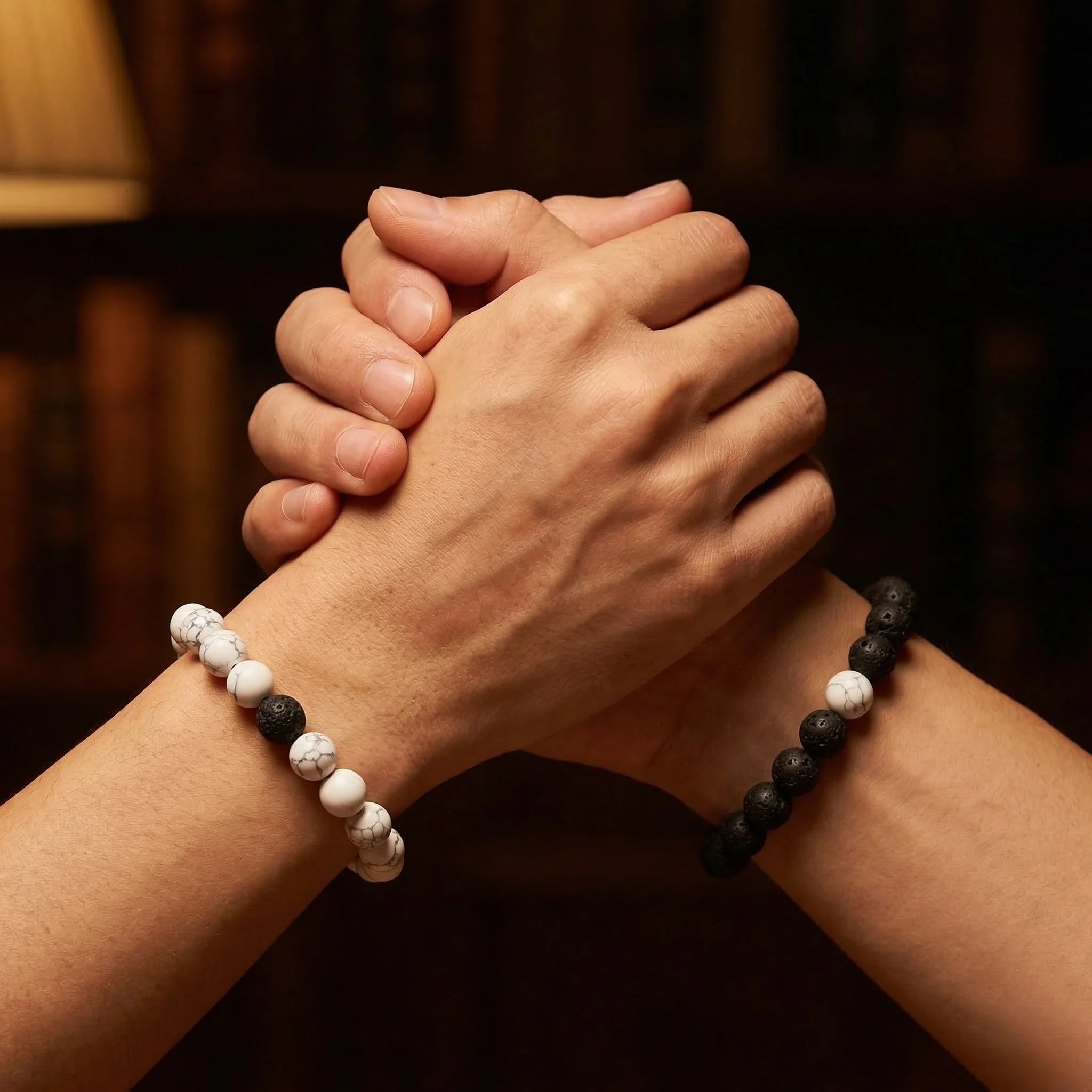 Two hands clasped together with black and white beaded bracelets on a blurred background