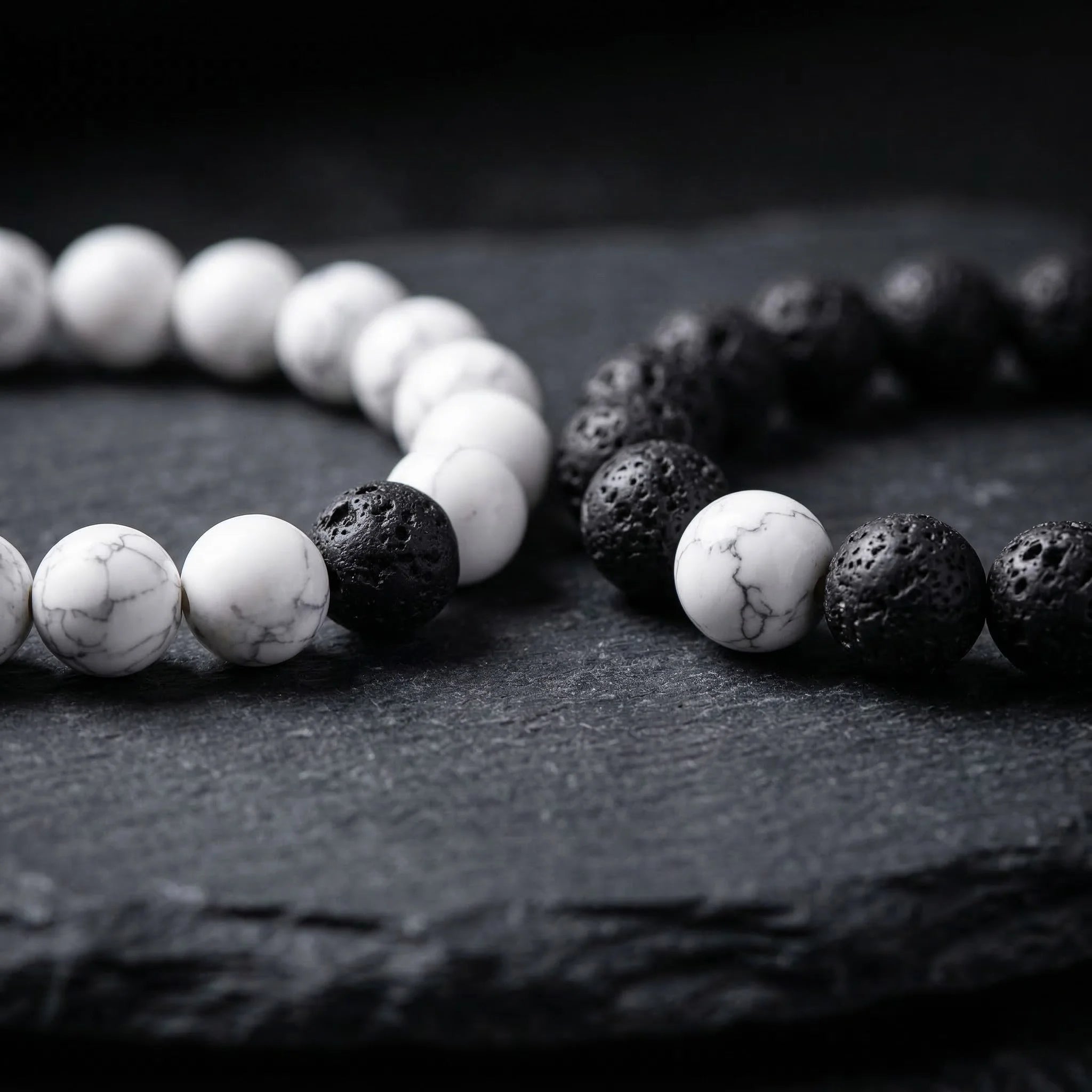 Two bracelets made of white beads and black volcanic stones on a dark surface