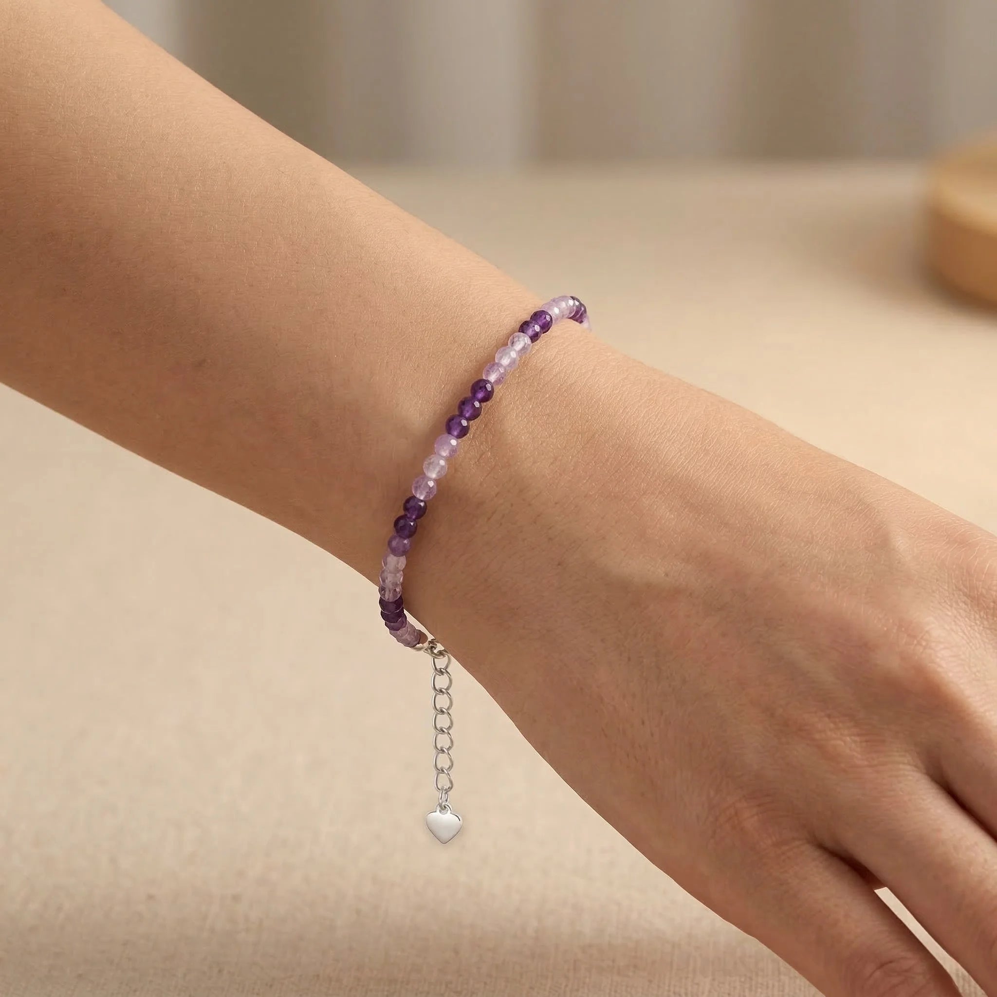 Purple beaded bracelet with a heart charm on a wrist against a neutral background