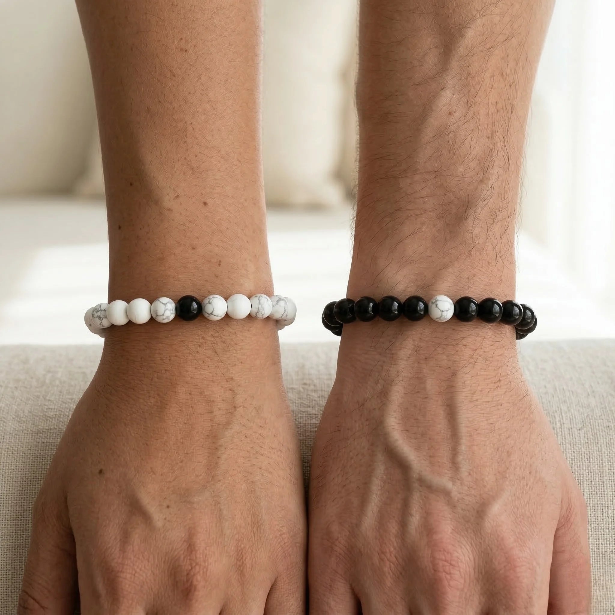 Two wrists wearing beaded bracelets on a neutral background