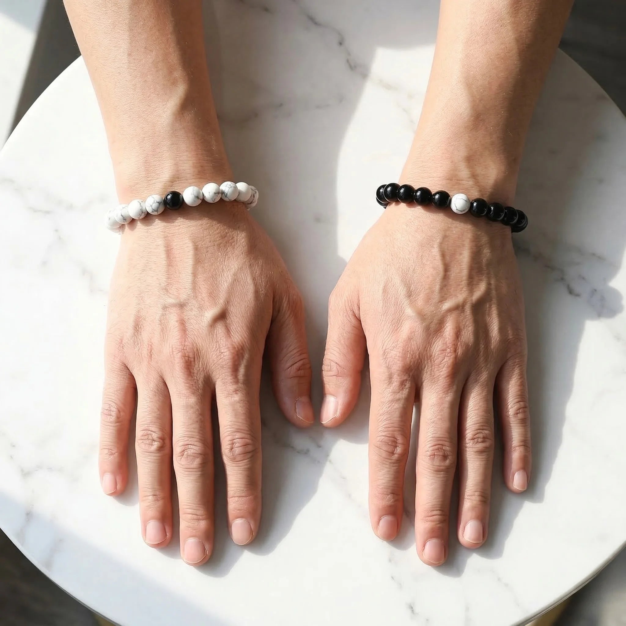 Two hands wearing beaded bracelets on a marble surface