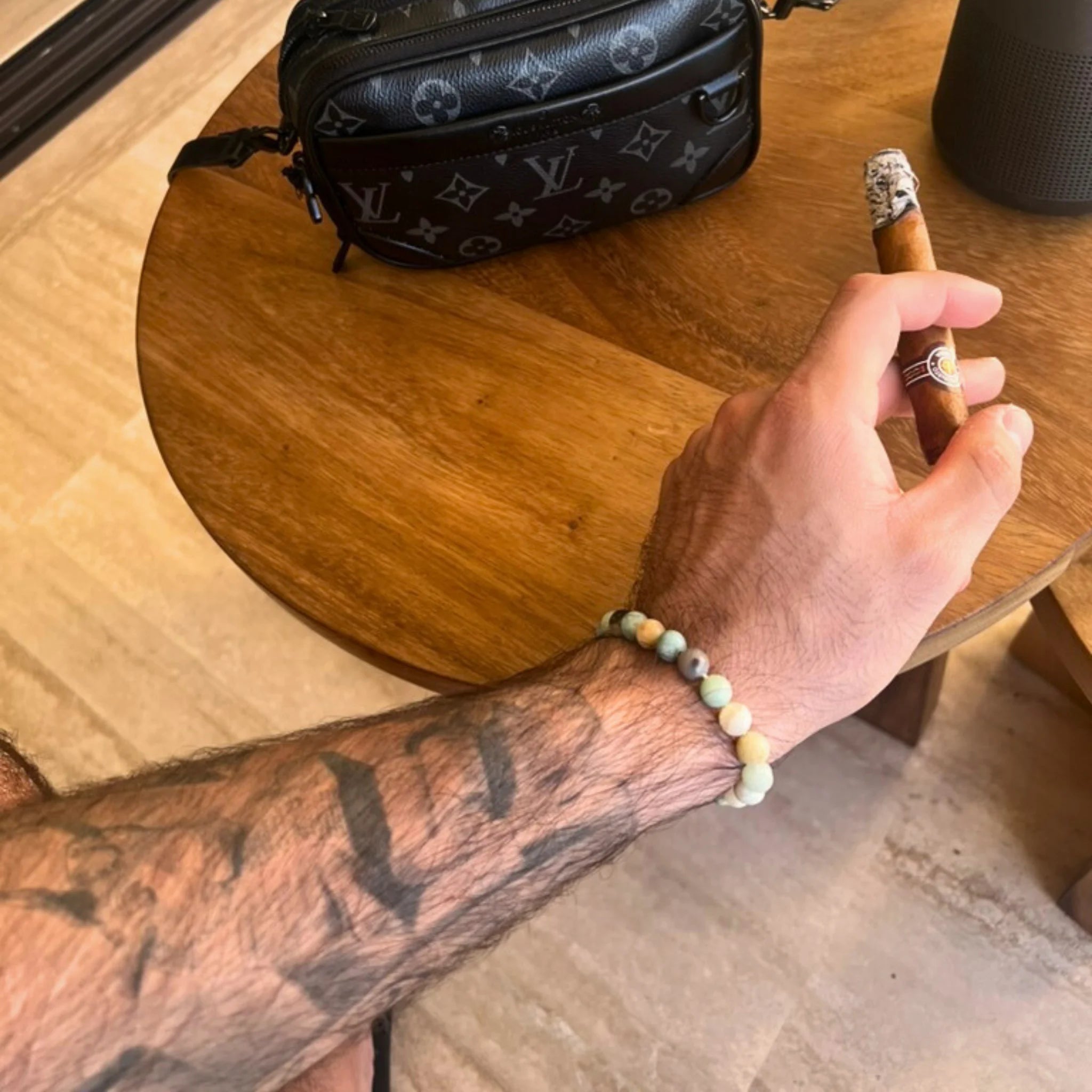 Gemstone4K amazon stone bracelet worn on wrist near beach or sunlight, showing aqua tones and reflective polish.