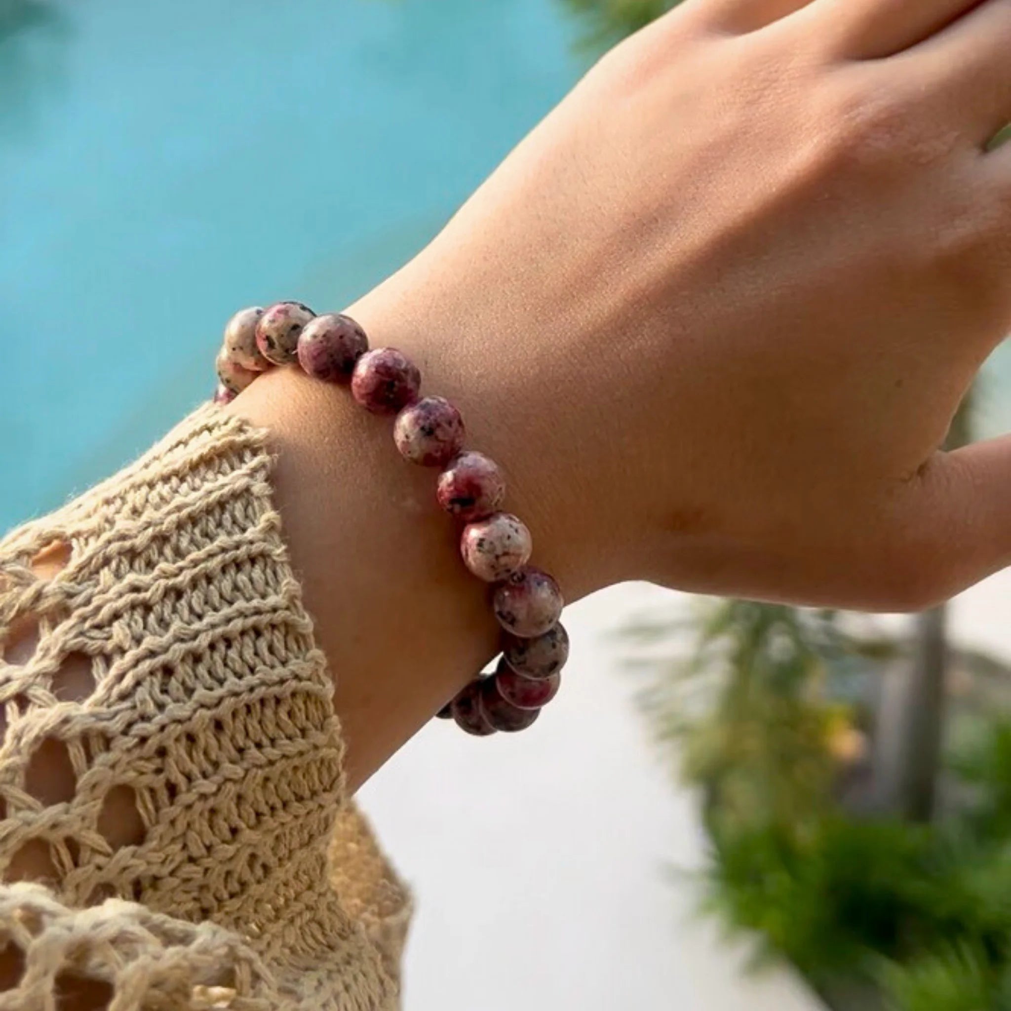 Gemstone4K rhodonite bracelet worn on wrist outdoors, showing pink tones and smooth polished surface.