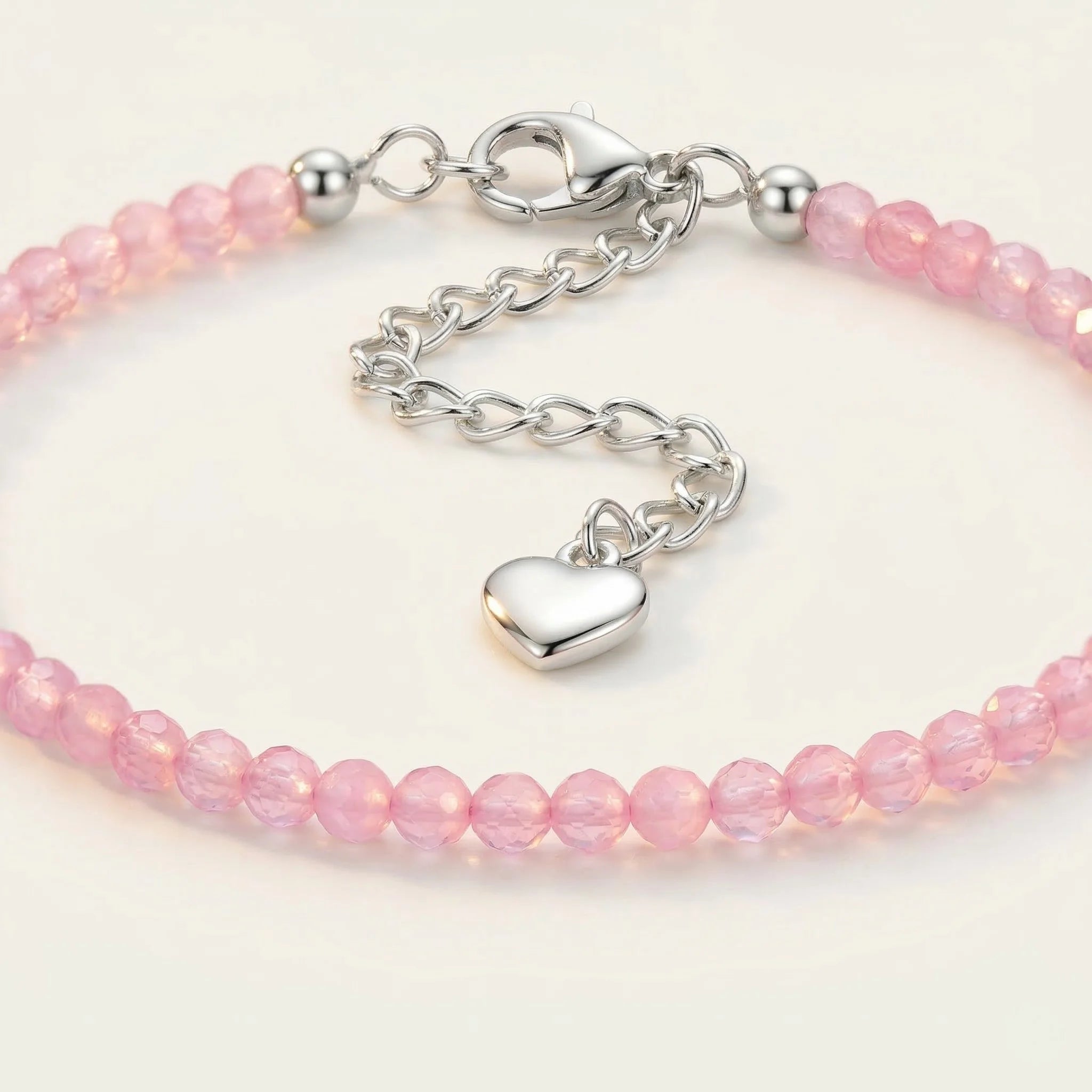 Pink beaded bracelet with a silver heart charm on a light background